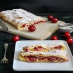 Strudel on a marble board with two slices cut on a square plate.