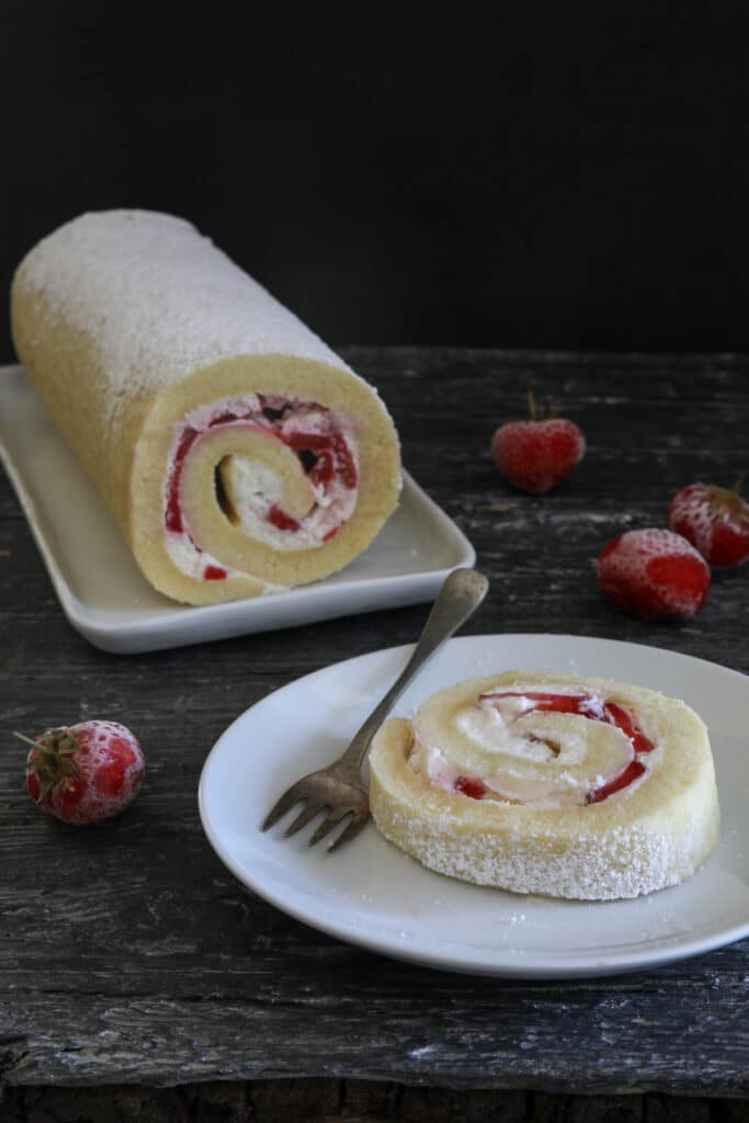 Cake roll on a white plate with a slice on a small white plate.