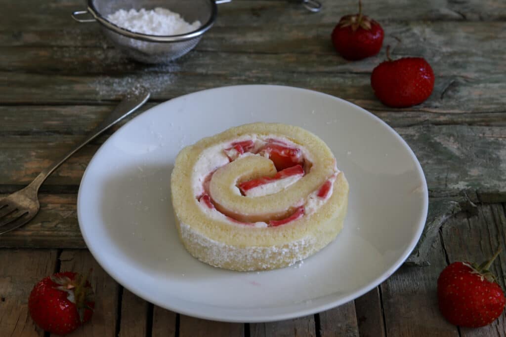 A slice of strawberry cake roll on a white plate.