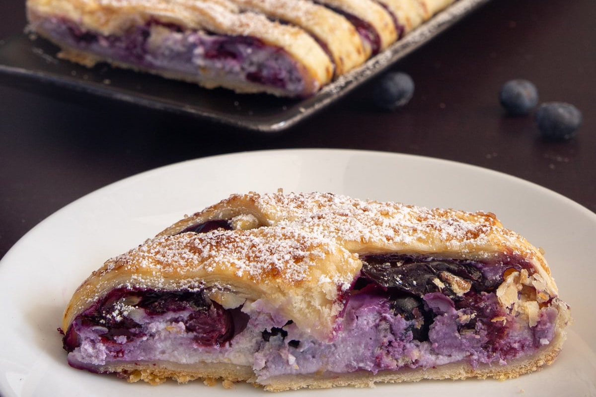 Blueberry strudel on a black dish with a slice cut on a white plate.