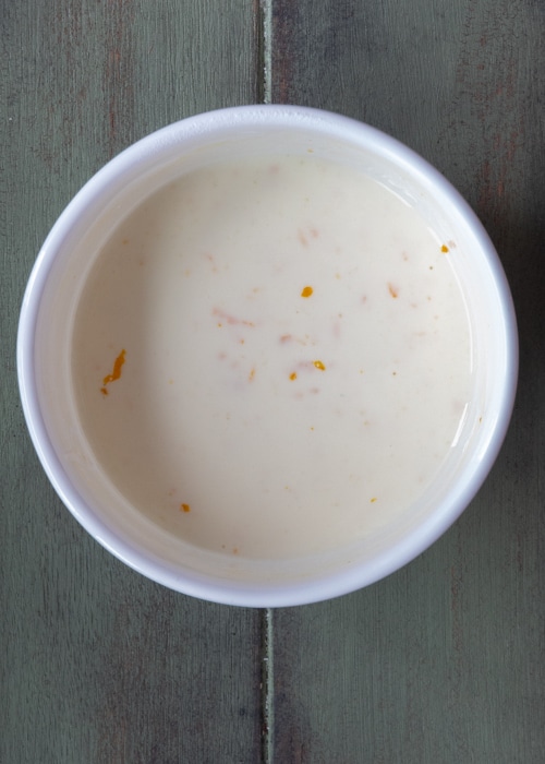 Orange juice, yogurt and zest mixed in a white bowl.