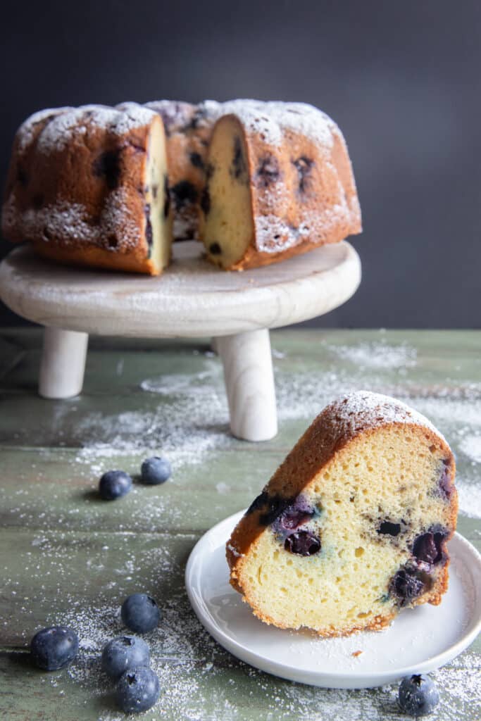 Cake on a cake stand with a slice on a white plate.