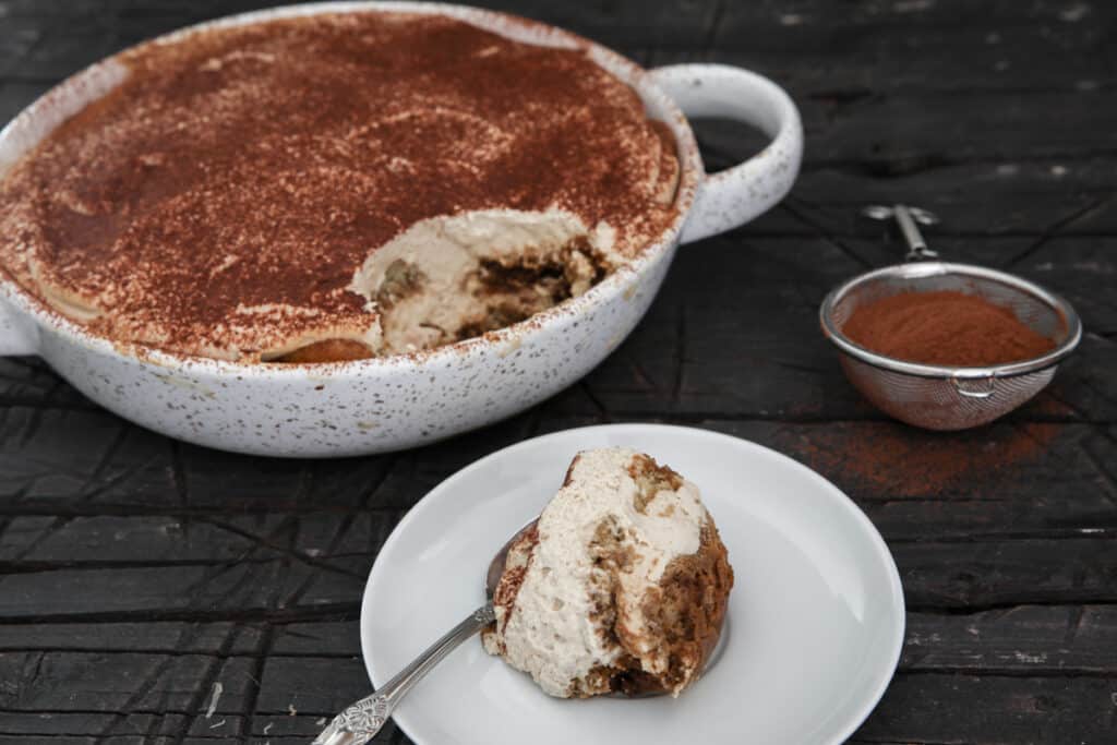 Tiramisu in a white baking dish and some on a spoon.