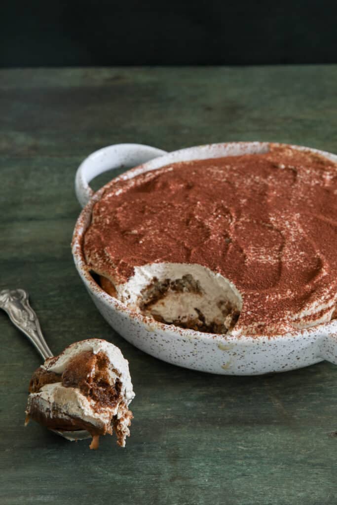 Tiramisu in a white baking dish and some on a spoon.