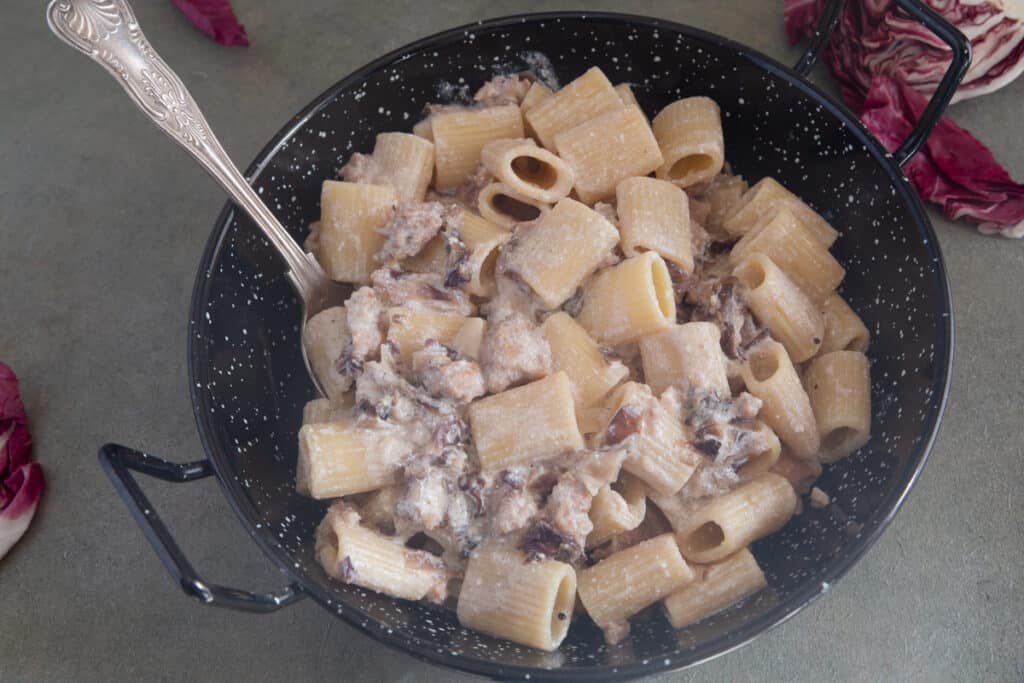 Pasta in a black pan with a spoon.