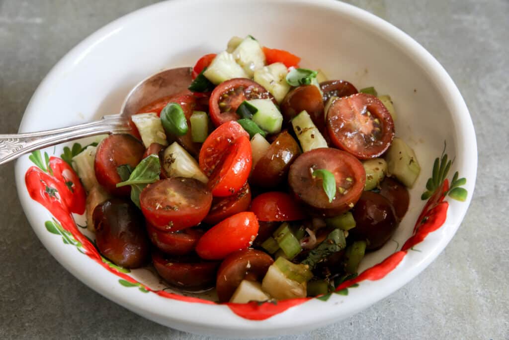 Chopped tomatoes and veggies in a white bowl with a silver spoon.