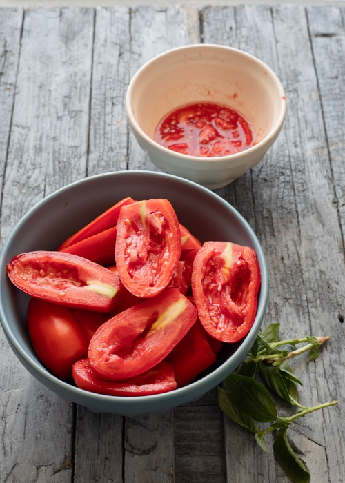 Halved tomatoes in a bowl with seeds in another small white bowl.