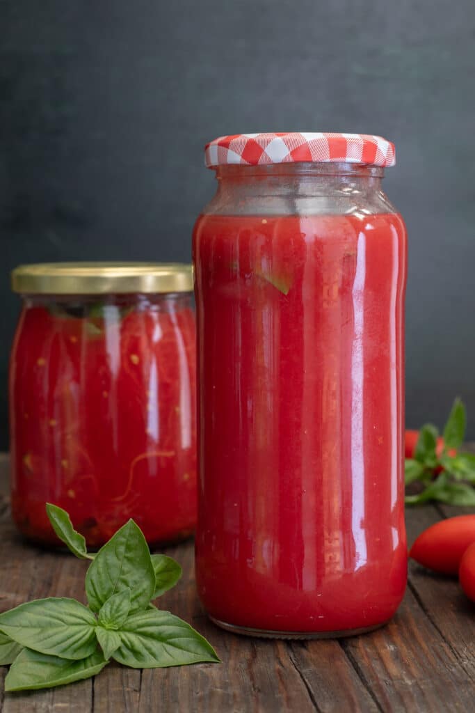 Jarred tomatoes on a wooden board with fresh basil.