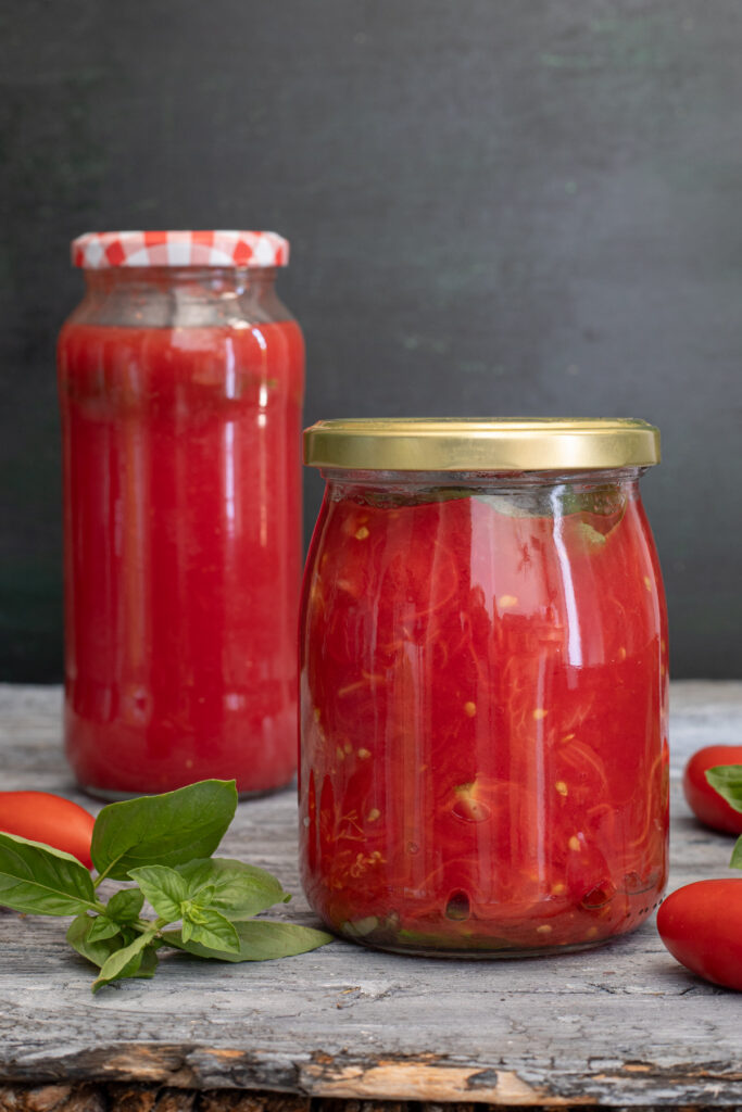 Jarred tomatoes on a wooden board with fresh basil.