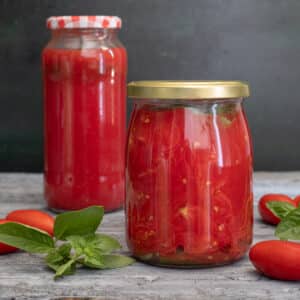 Jarred tomatoes on a wooden board with fresh basil.