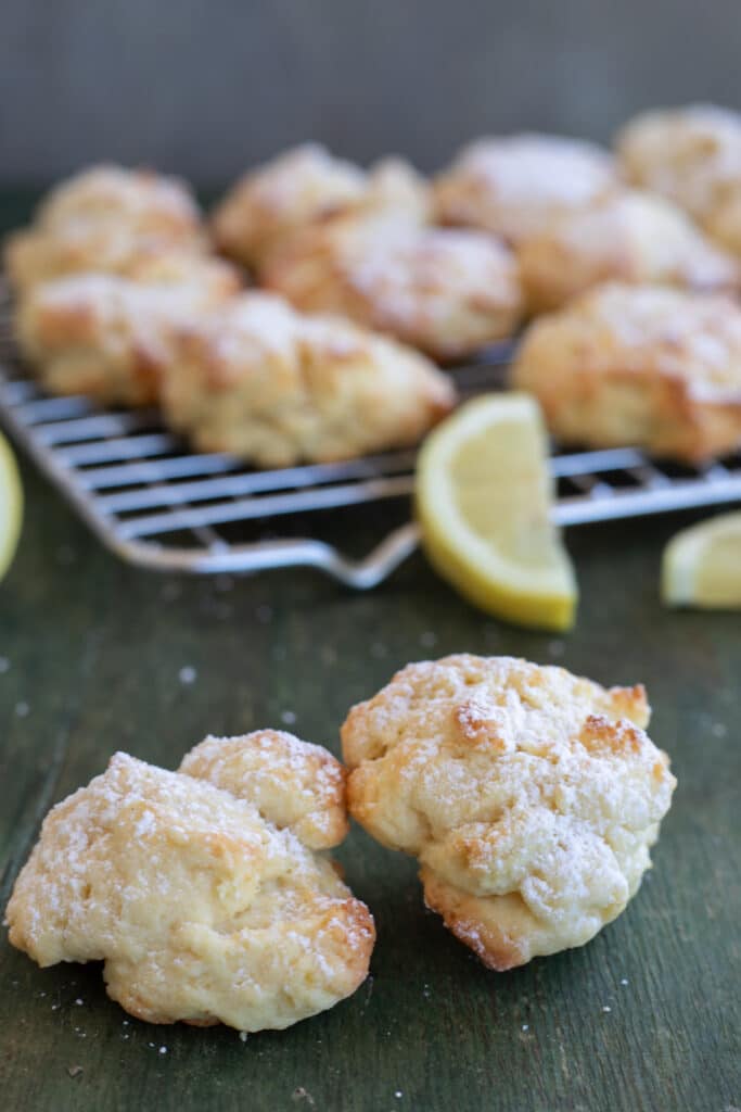 Two lemon ricotta cookies on a board and some on a wire rack.