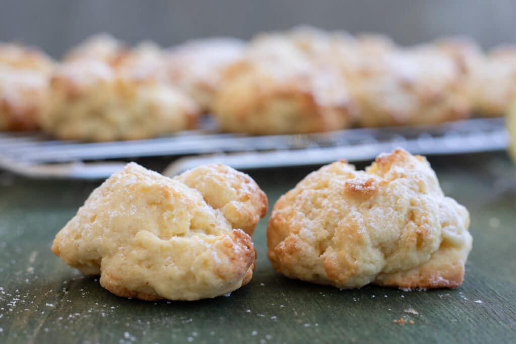 Two lemon ricotta cookies on a board and some on a wire rack.