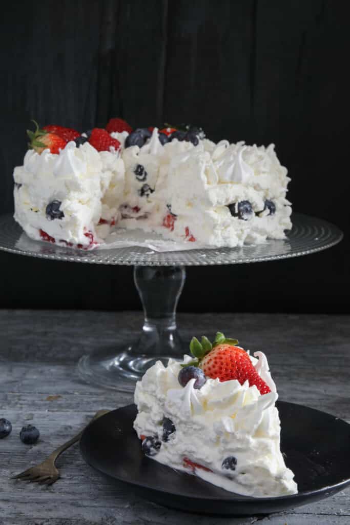 Cake on a glass cake stand with a slice on a black plate.