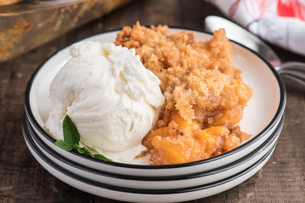 Peach crumble with ice cream on a white plate.