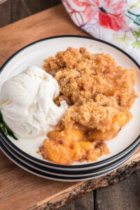 Fresh peach crumble on a white plate with a scoop of ice cream.