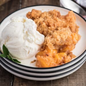 Fresh peach crumble on a white plate with a scoop of ice cream.