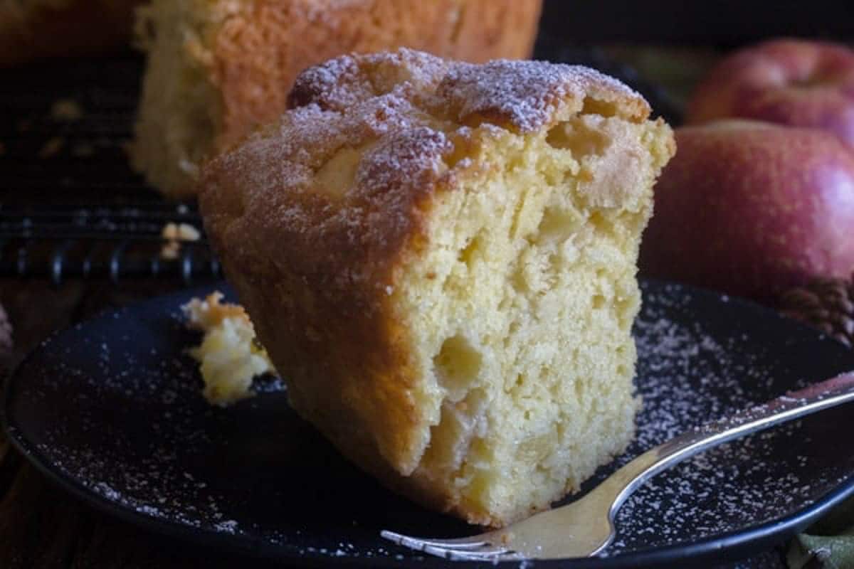 A slice of apple cake on a black plate with a silver fork.