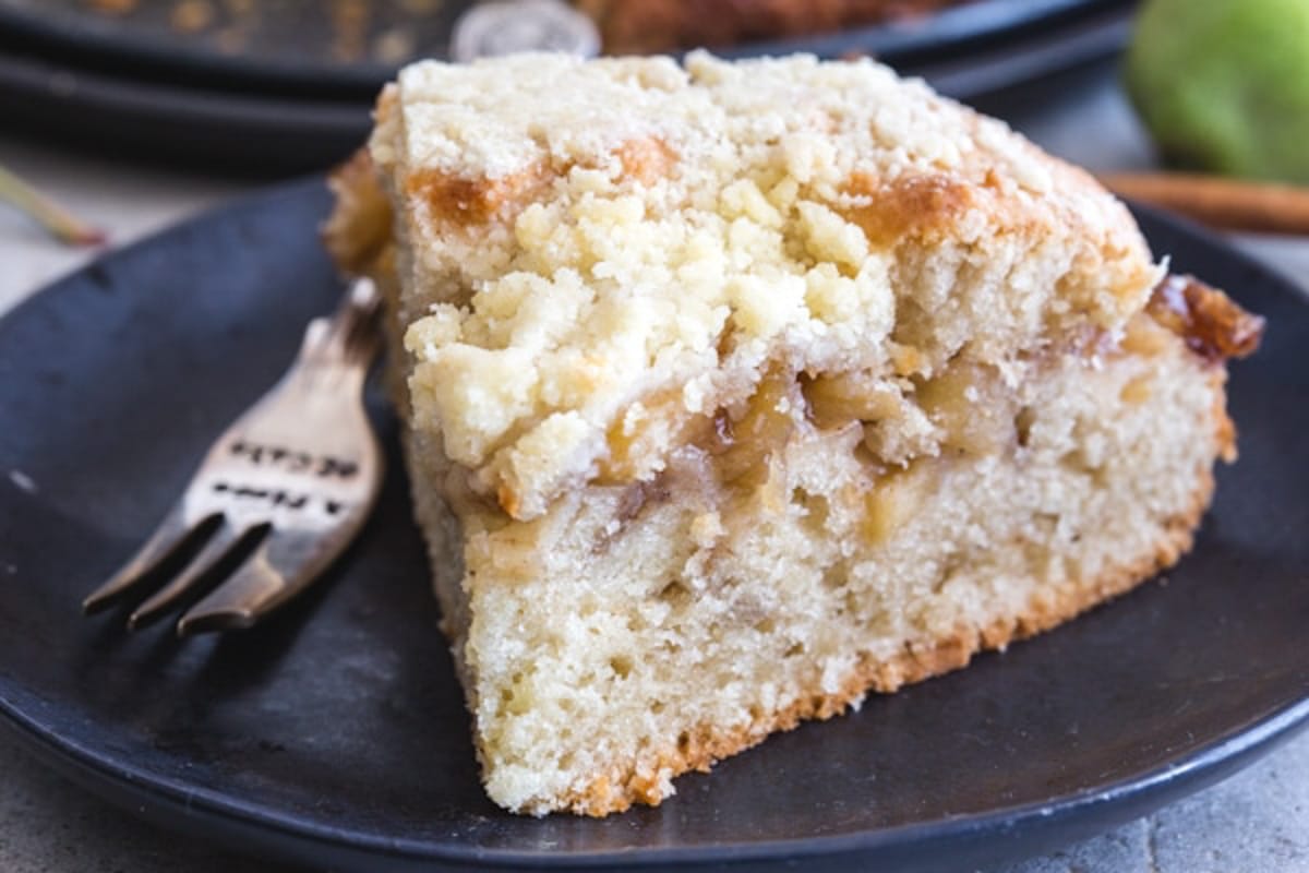 A slice of apple cake on a black plate with a fork.