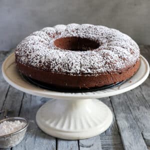 The cake dusted with powdered sugar on a white cake pan.