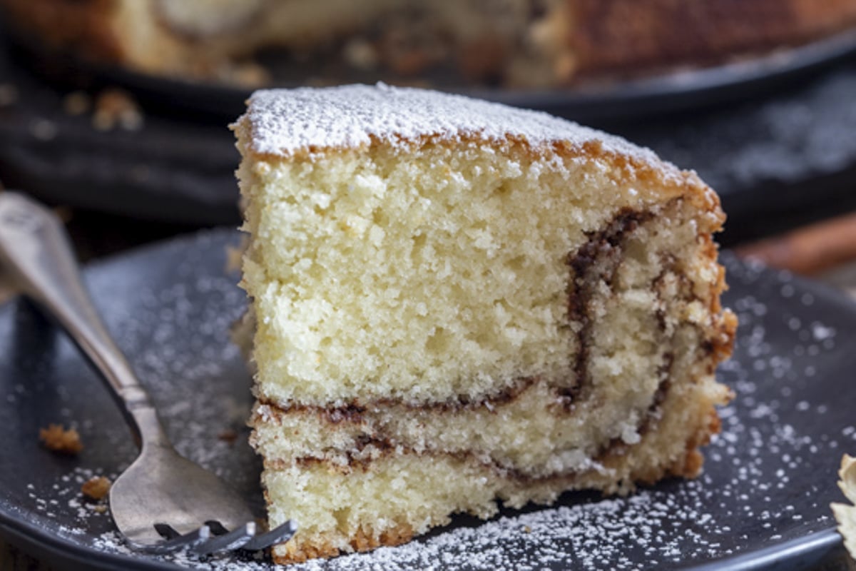 A slice of cinnamon cake on a black plate.