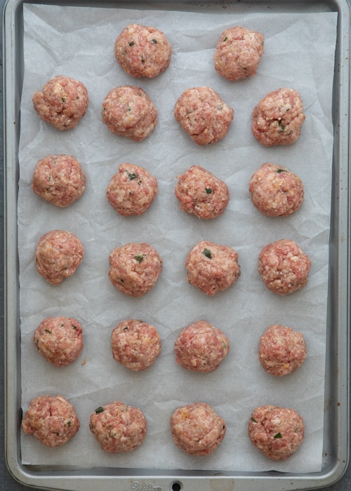 The meat formed into meatballs on a parchment paper lined baking sheet.