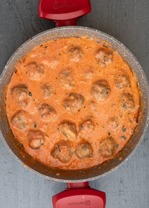 The meatballs cooked in the sauce in the red pan.