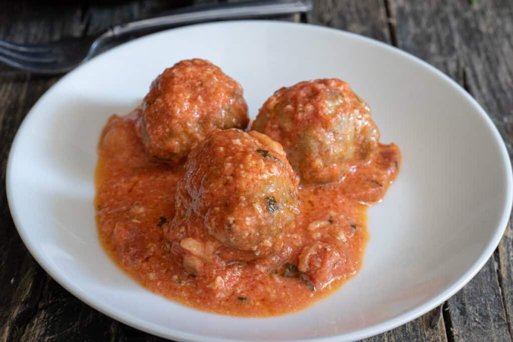 Three meatballs on a white plate.