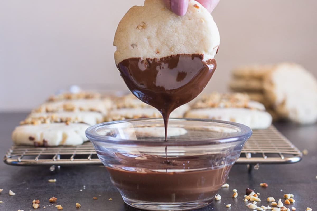 Dipping a walnut shortbread cookie in melted chocolate.