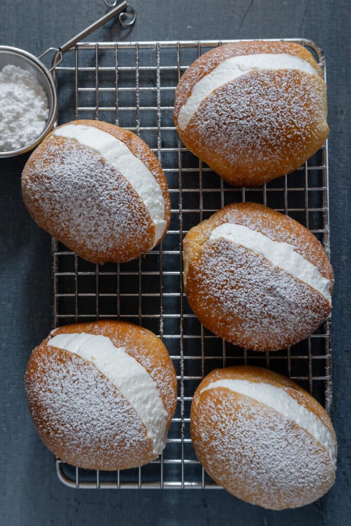 Five cream filled buns on a wire rack.