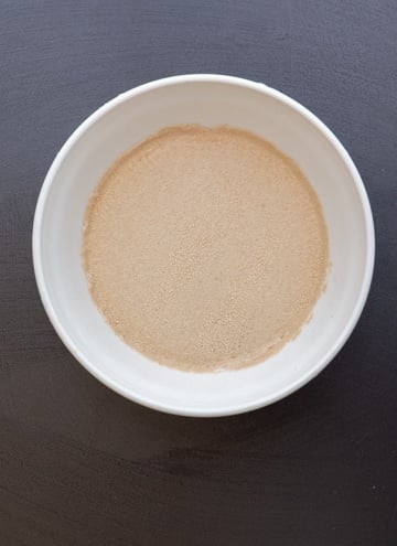 The yeast, water and sugar in a white bowl.