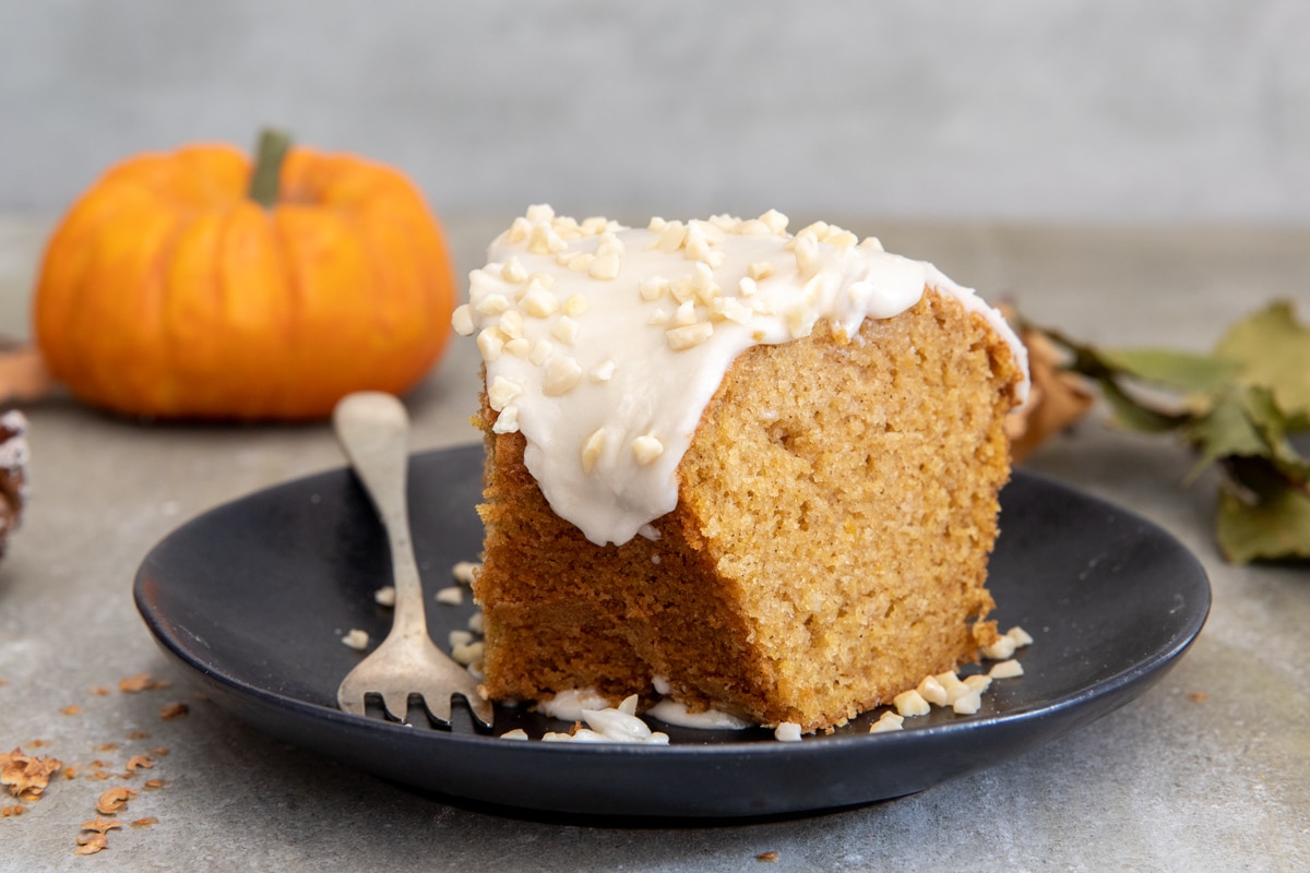 A slice of glazed pumpkin cake on a black plate.