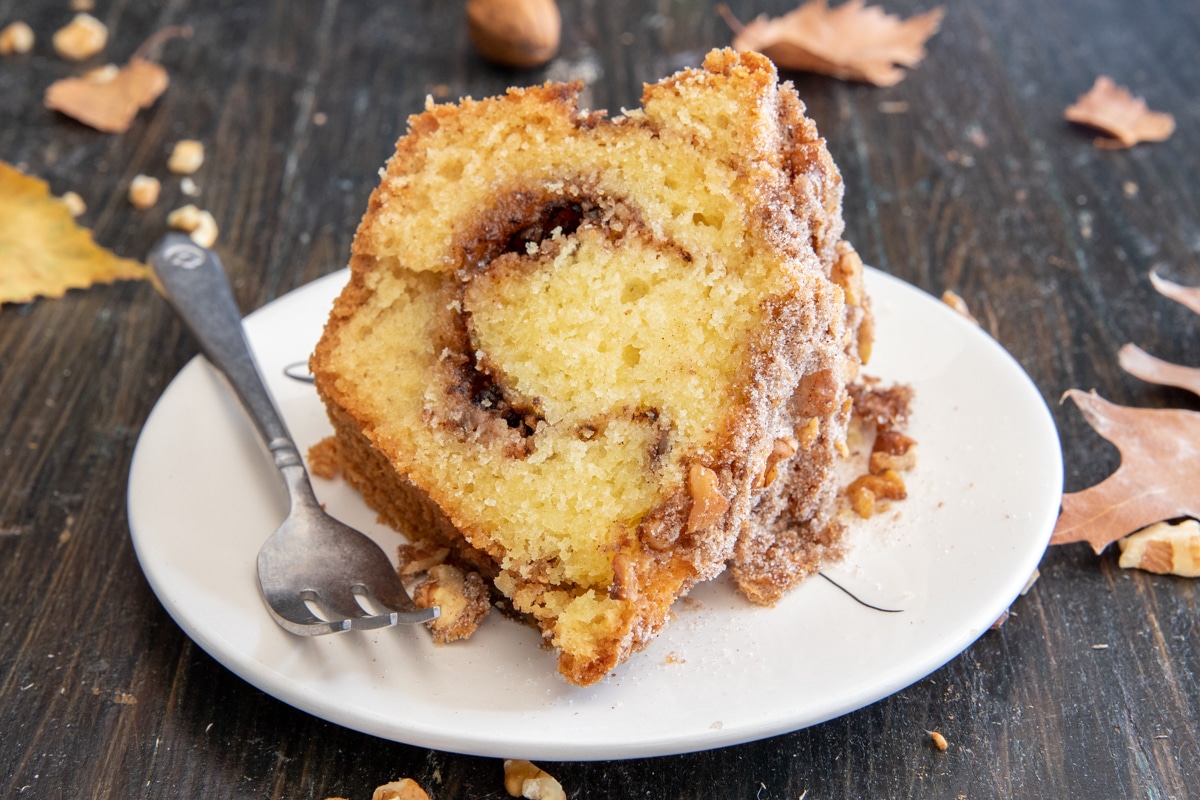 A slice of cinnamon walnut cake on a white plate with a fork.