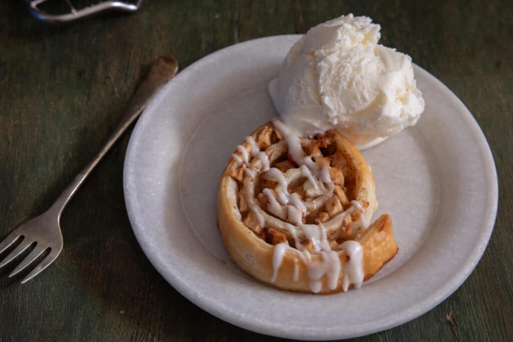 An apple roll up with a scoop of ice cream on a white plate.