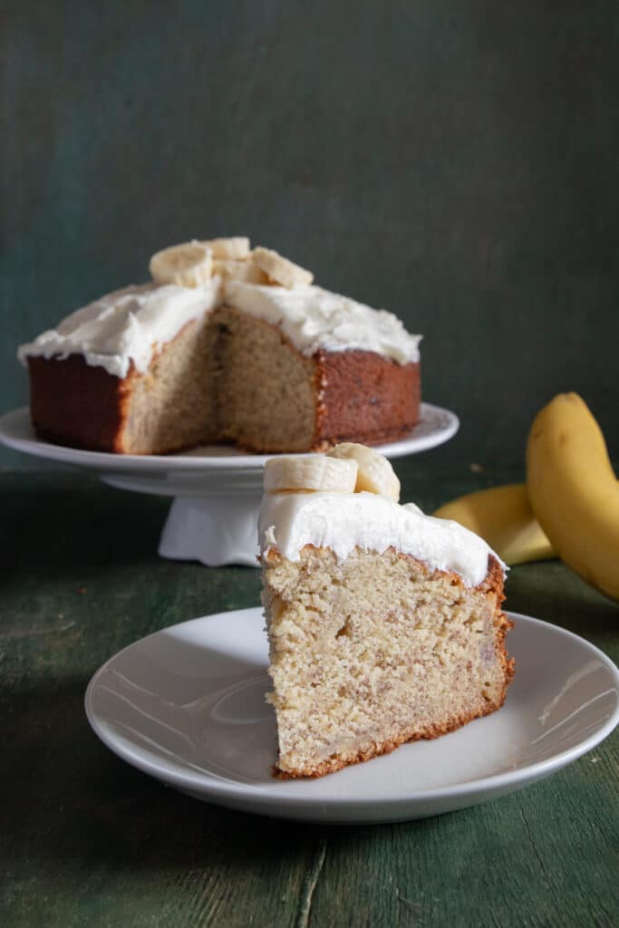 Cake on a cake stand with a slice on a white plate.