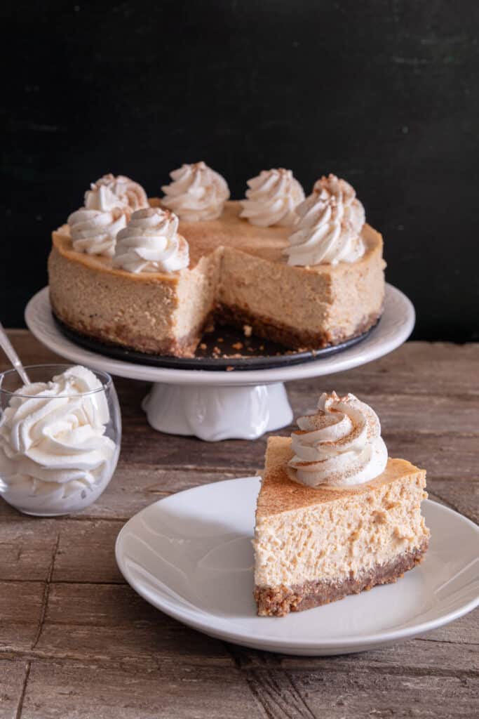 Pumpkin cheesecake on a white cake stand with a slice on a white plate.