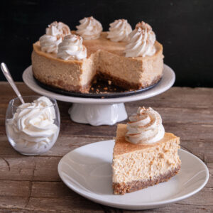 Pumpkin cheesecake on a white cake stand with a slice on a white plate.