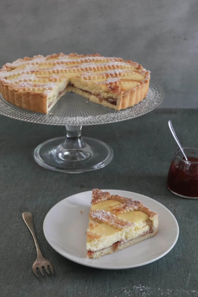 Crostata on a glass cake stand and a slice on a white plate.