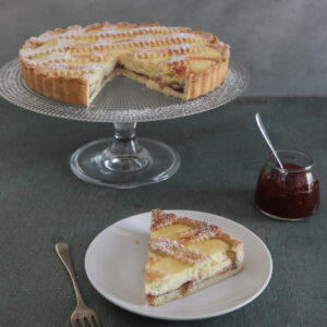 Crostata on a glass cake stand and a slice on a white plate.