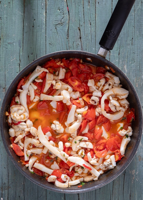 The calamari added to the tomatoes in the pan.