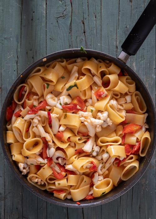 The pasta added to the pan with the calamari and tomatoes.