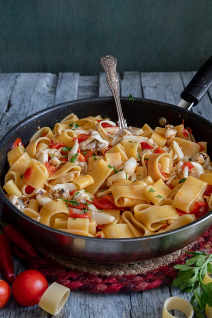 The calamarata pasta in a black pan with a silver spoon.