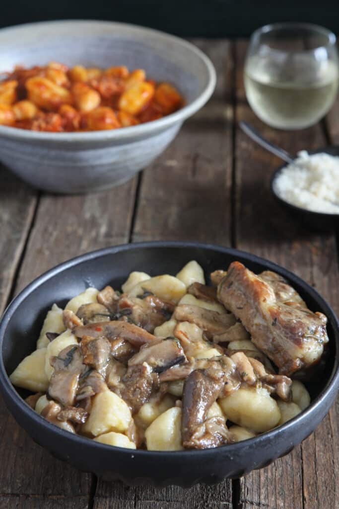 Gnocchi in a black bowl and in a blue bowl, with mushrooms and with sauce.