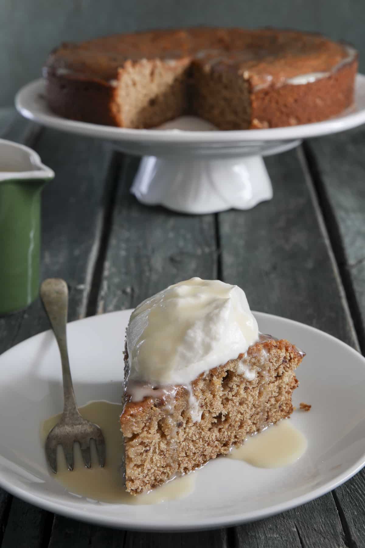 Sticky toffee pudding cake on a cake stand and a slice on a white plate.