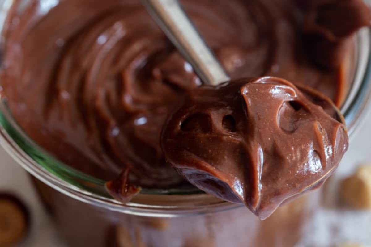 Hazelnut cream spread in a jar and some on a spoon.