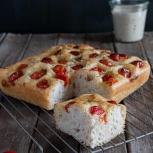 Tomato focaccia on a wire rack with a slice cut.