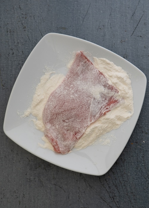 Dredging the meat in flour.