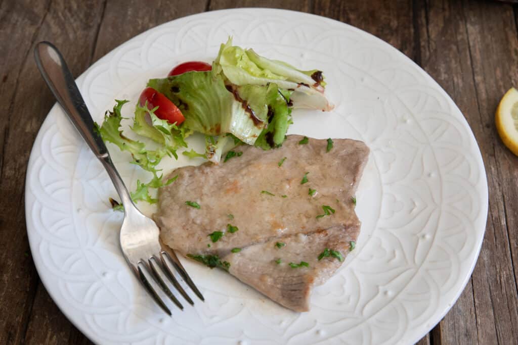 A slice of veal on a white plate with some salad.