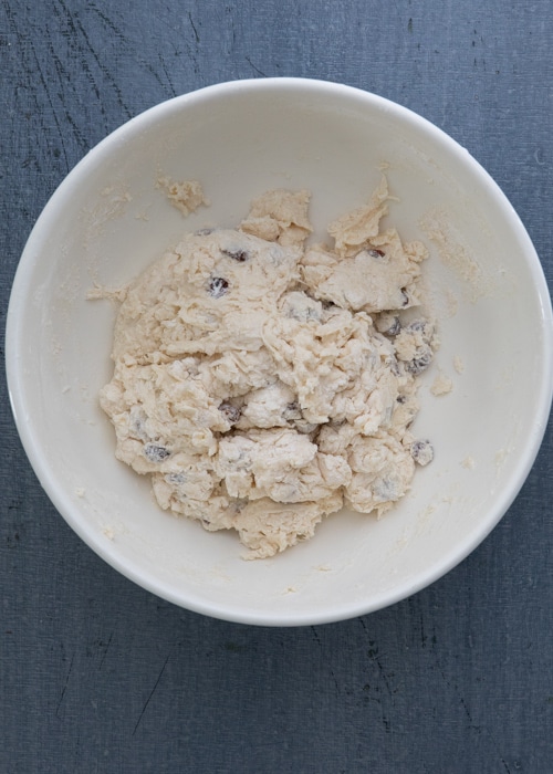 Mixing the wet and dry to form a shaggy dough in a white bowl.