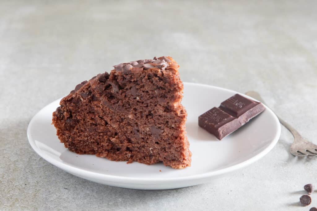 A slice of cake on a white plate with chocolate.