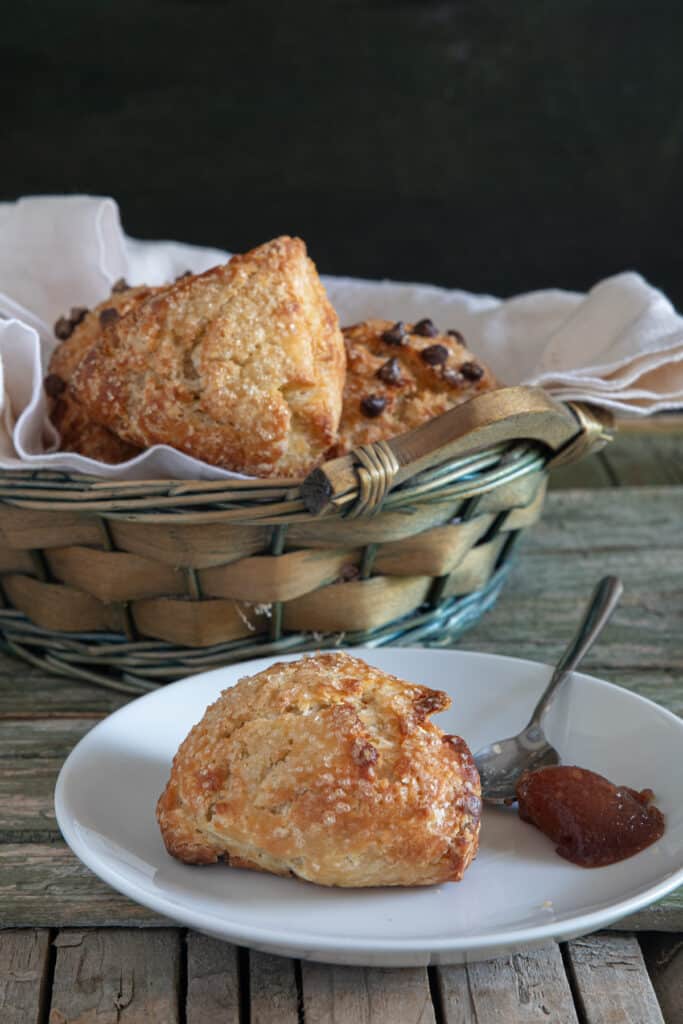 Scones in a basket and one on a plate with some jam.